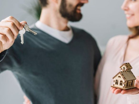 Happy couple holding house keys and a miniature home, symbolizing new home ownership.