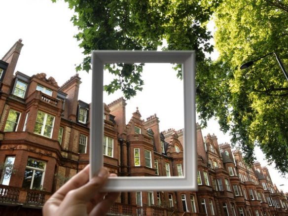 View of ornate red brick buildings through a frame with green foliage above, creating an artistic perspective.