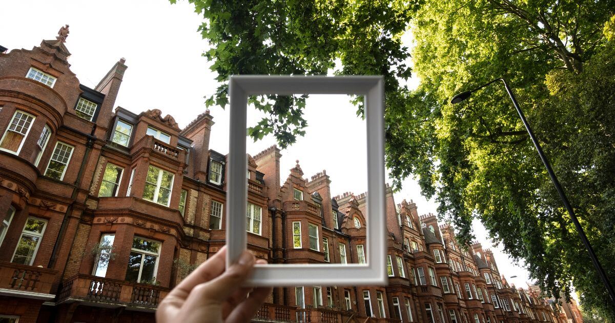 View of ornate red brick buildings through a frame with green foliage above, creating an artistic perspective.