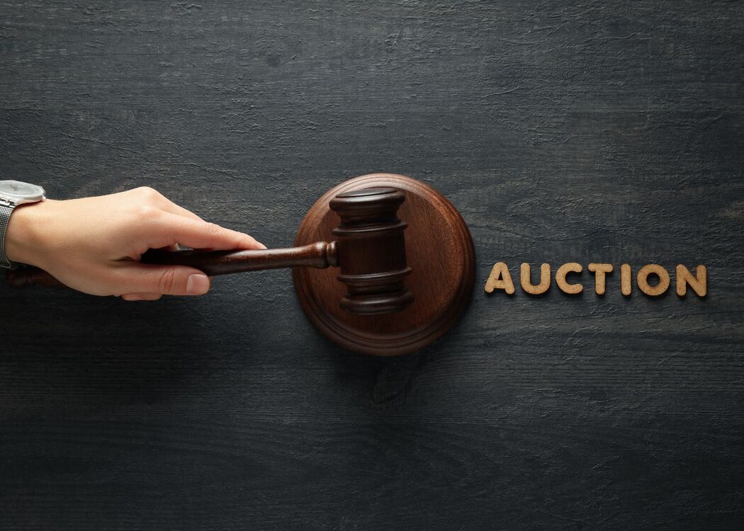 Hand holding a gavel near the word auction on a dark wooden surface.