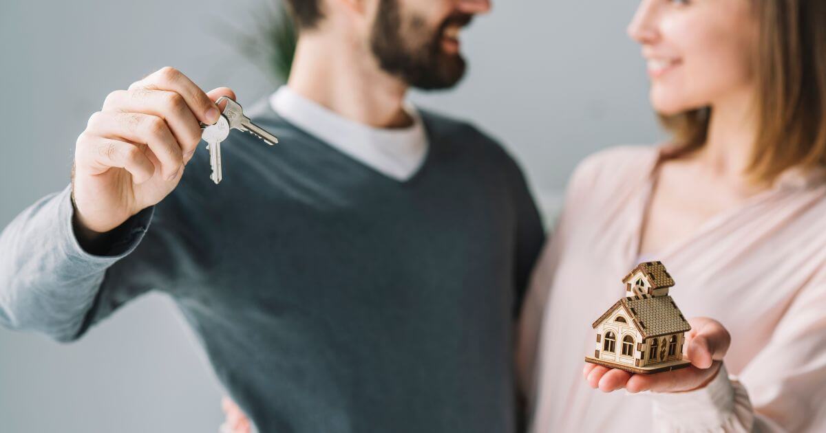 Happy couple holding house keys and a miniature home, symbolizing new home ownership.