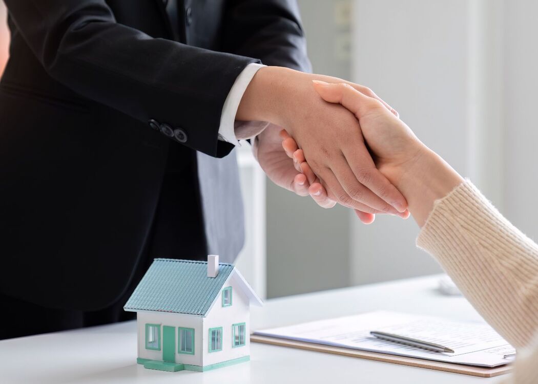 Handshake over real estate agreement with house model on desk, symbolizing a successful property transaction.