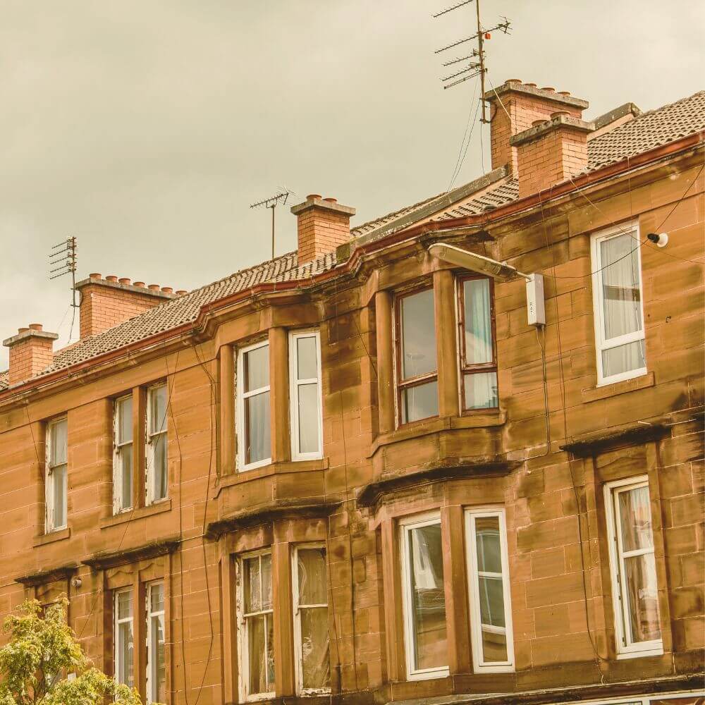 Victorian-style brick building with multiple windows and TV antennas under an overcast sky.