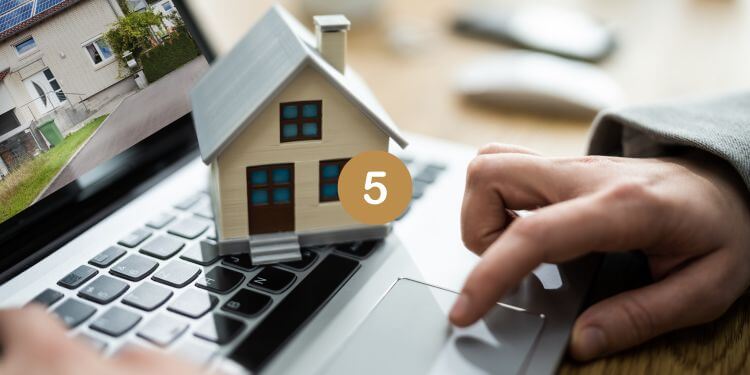 Person browsing real estate options on a laptop, with a house model representing online property search.