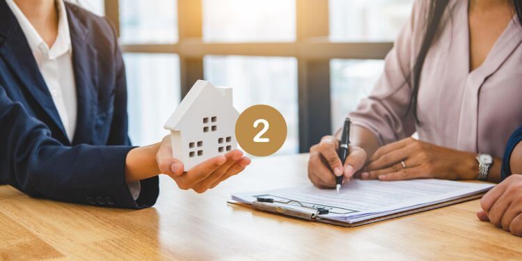 Real estate agreement signing with house model and clipboard on desk.